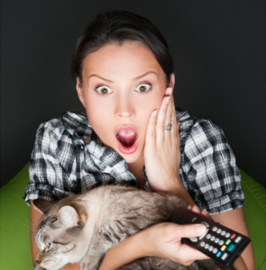 woman shocked watching tv holding a cat